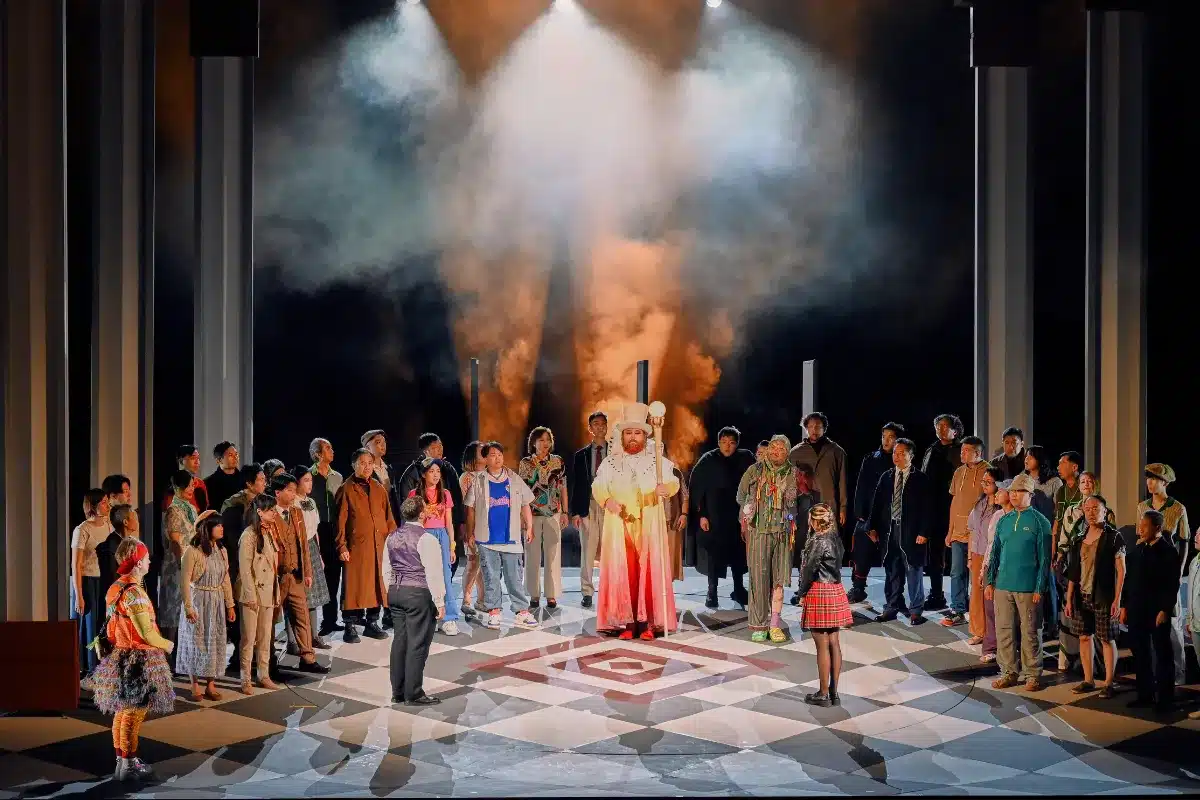 The cast of the play stands together on stage, dressed in costumes, ready to perform for the audience.