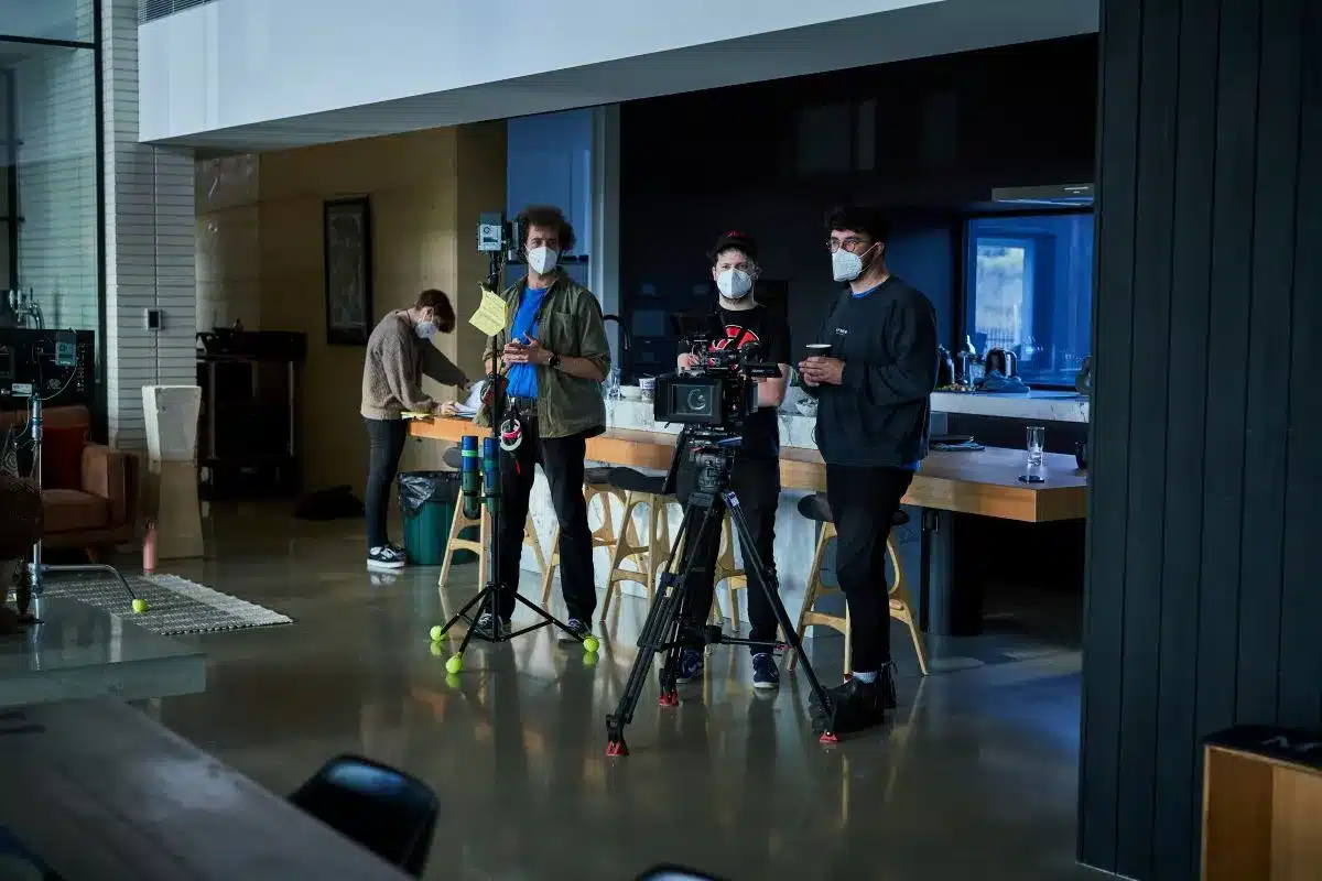 Three individuals set up a camera on a tripod in a well-lit room, preparing for a photo shoot.