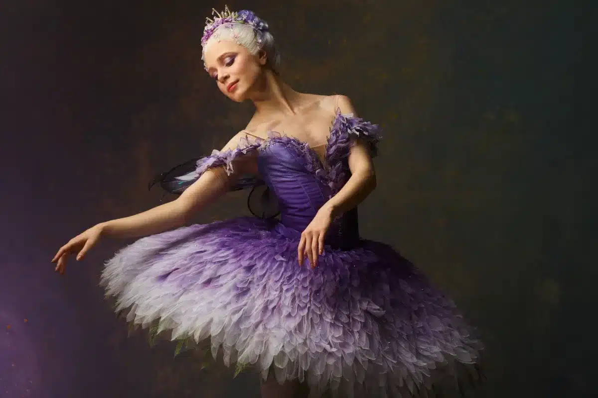 A ballerina wearing a purple tutu adorned with feathers, poised gracefully in an elegant dance position.
