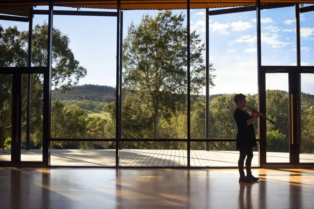 A person gazes out at a scenic landscape through large windows, standing in a well-lit interior space.