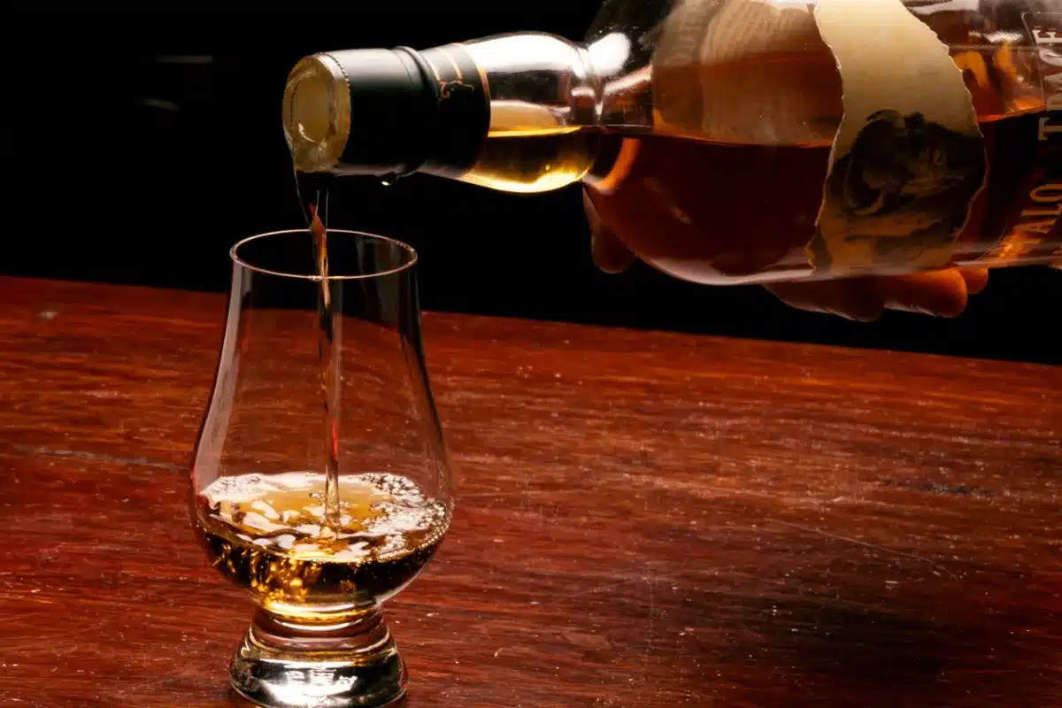 A person pouring whiskey from a bottle into a glass, with the liquid flowing smoothly into the clear glass.