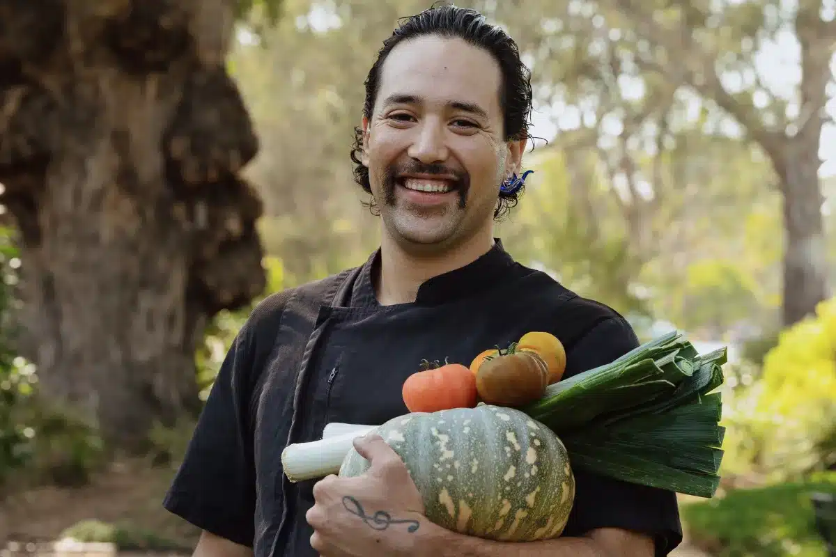A man in a chef's uniform proudly holds a large, fresh vegetable in his hands, showcasing his culinary expertise.