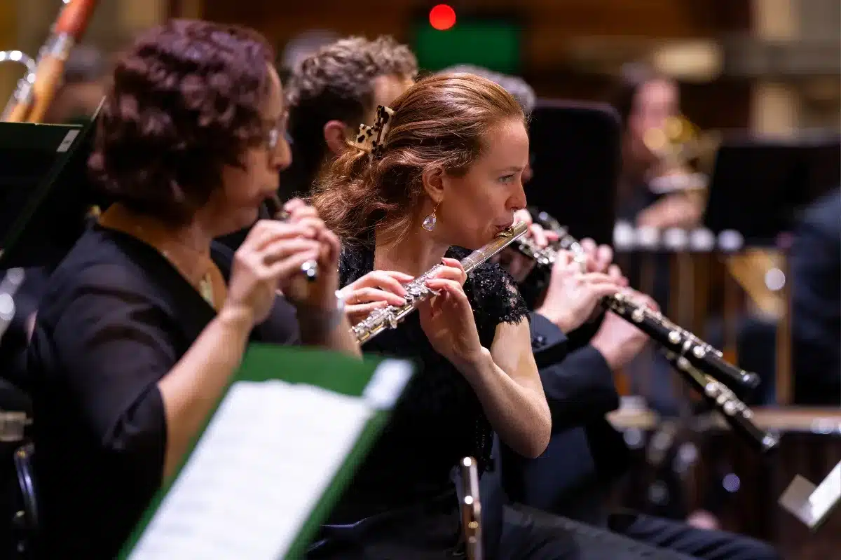 A group of musicians playing flutes together in an orchestra setting, focused on their performance.