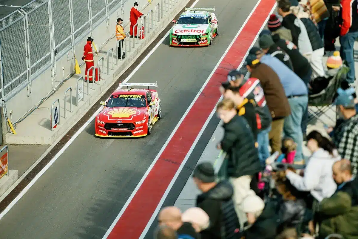Two cars race down a track while spectators watch from the sidelines, capturing the excitement of the event.