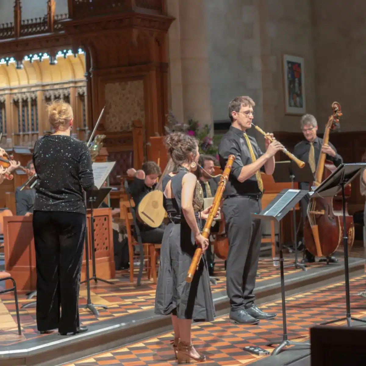 A diverse group of people stands together in front of a stage, engaged and looking towards the performance.
