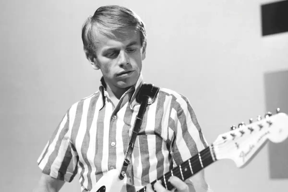 A man in a striped shirt passionately playing an electric guitar on stage.