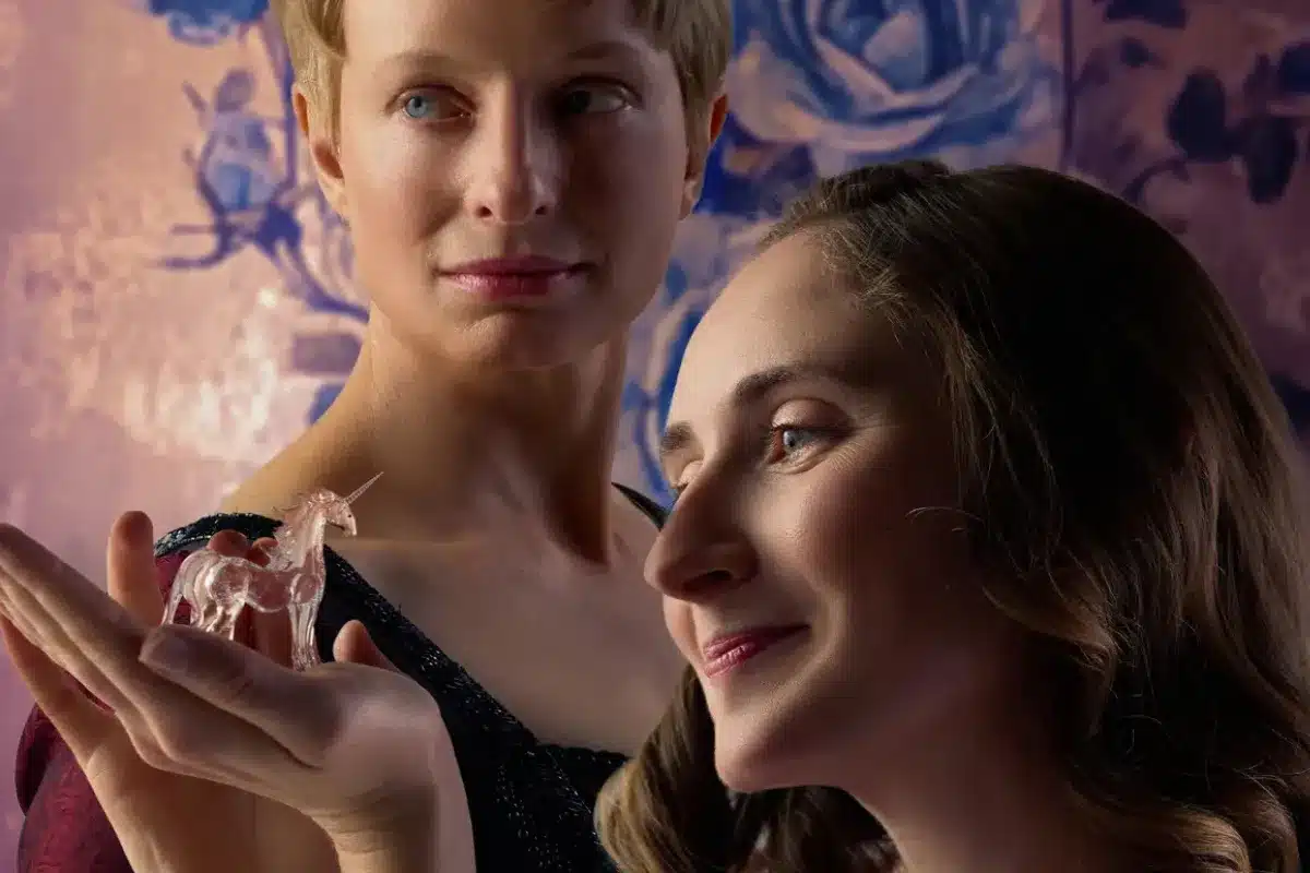 Two women hold a crystal together, standing in front of a vibrant blue wall.