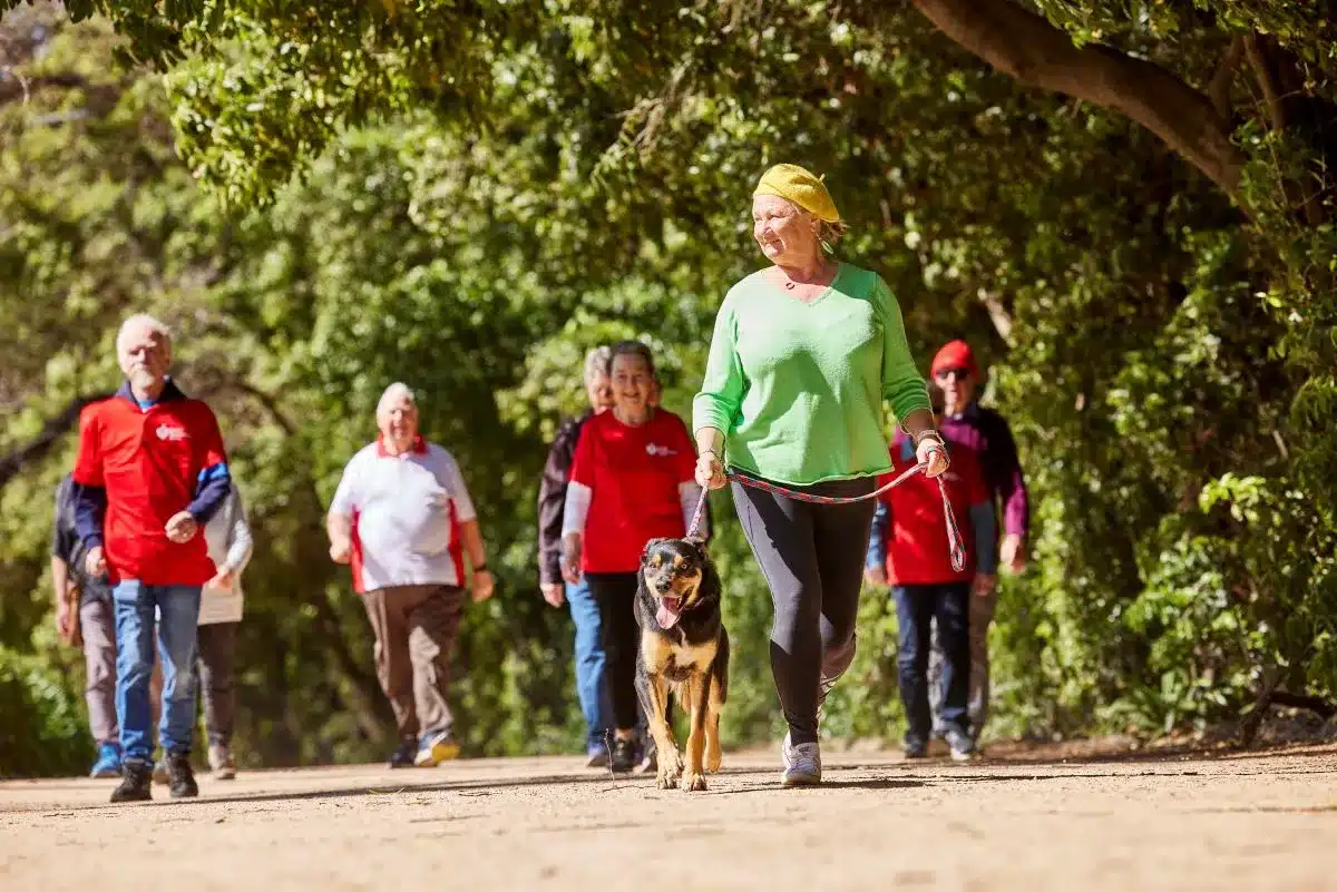 A group of people walking their dog along a scenic trail surrounded by trees and greenery.