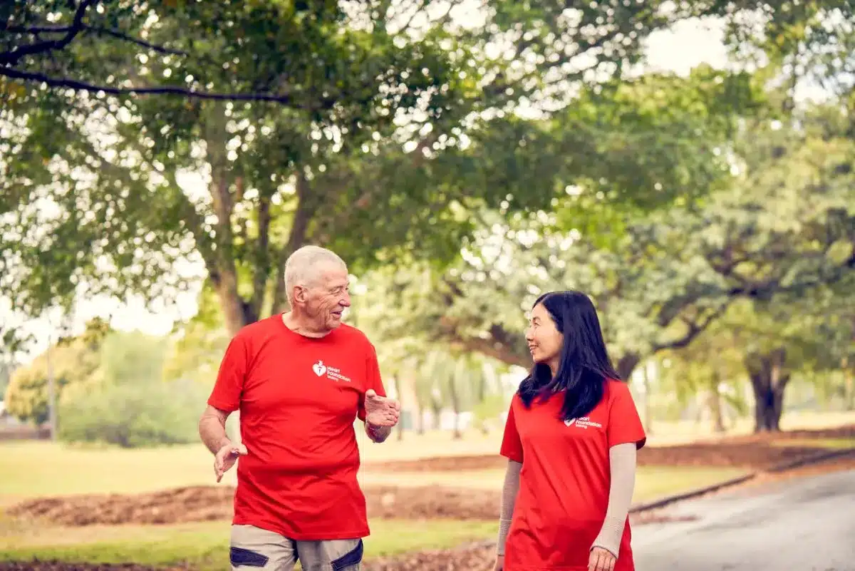 An older man and woman in red shirts engaged in conversation, smiling at each other in a friendly manner.