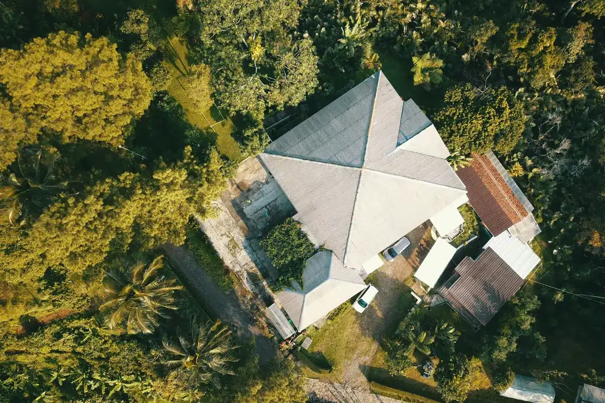 Aerial view of a house nestled among lush green trees, showcasing the natural surroundings and landscape.