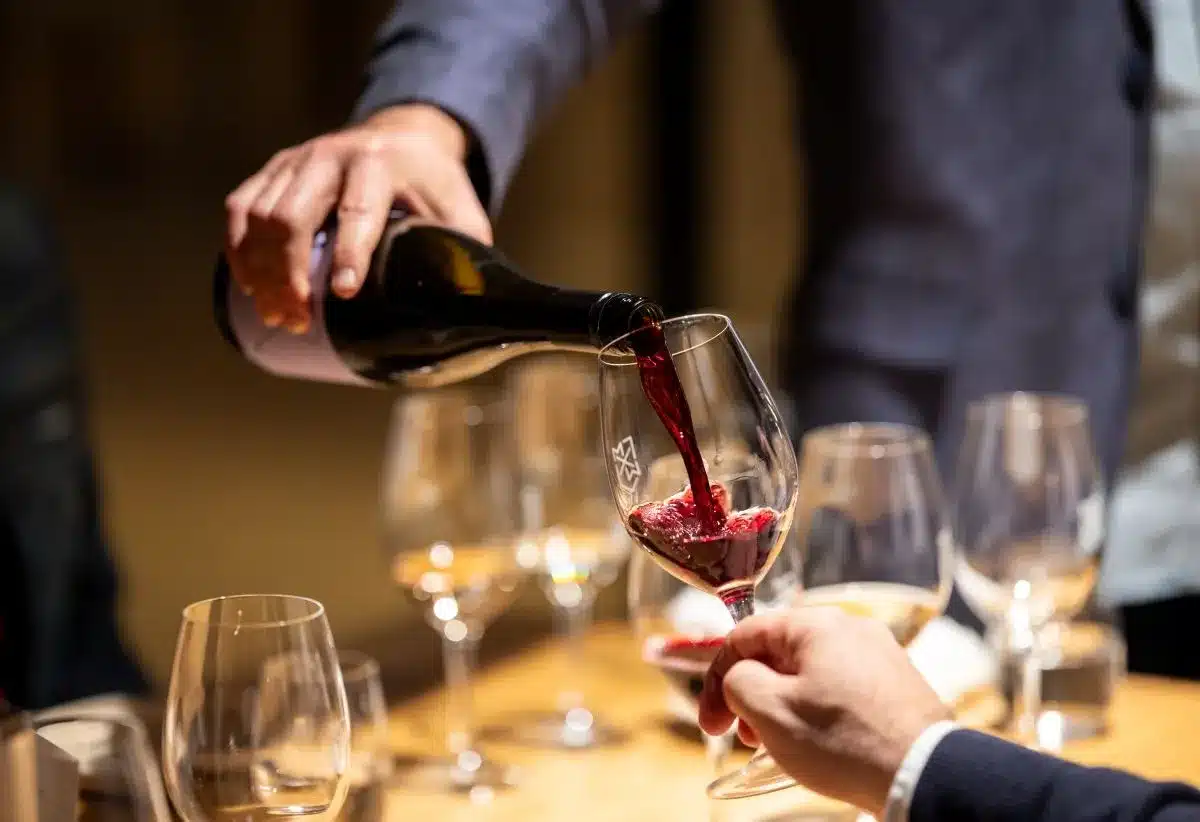 A hand pouring rich red wine into a clear glass, creating a splash.