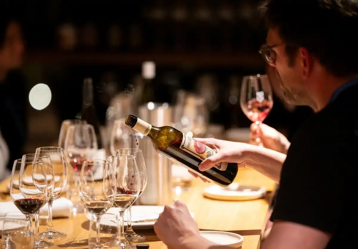 A man elegantly pours red wine into a glass at a beautifully set dining table.