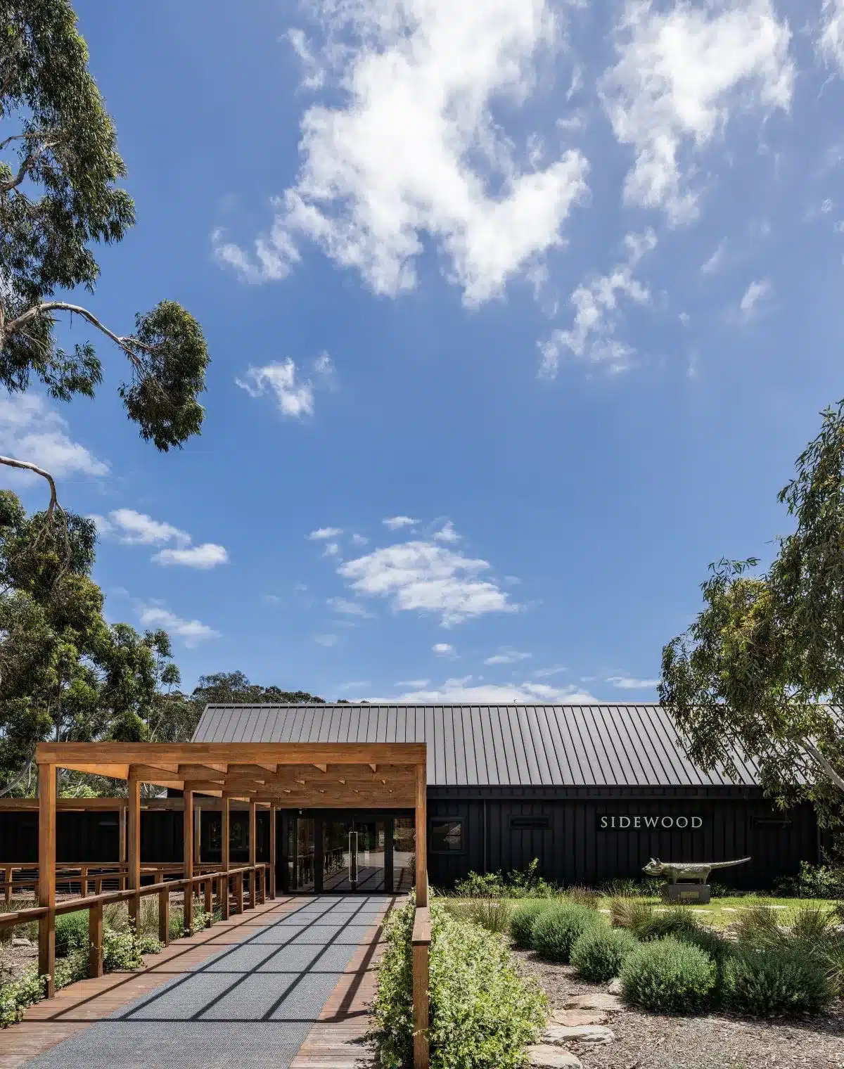The winery entrance is framed by lush trees and vibrant plants, creating a welcoming natural setting.