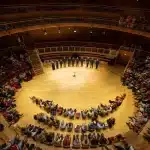 A large auditorium filled with people seated in rows of chairs, engaged in an event or presentation.