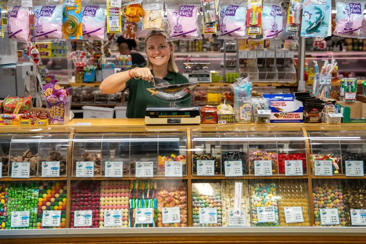 A woman in a store, looking at merchandise on shelves, with shopping carts visible in the background.