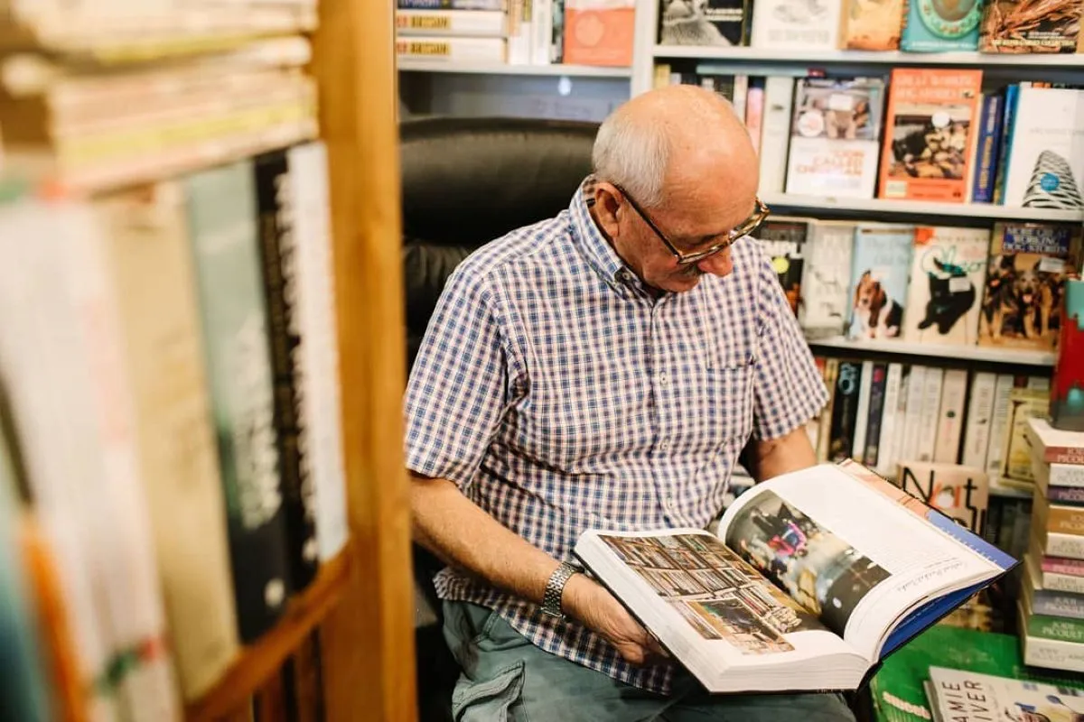 An older man seated in a chair, deeply focused on reading a book in a cozy indoor setting.