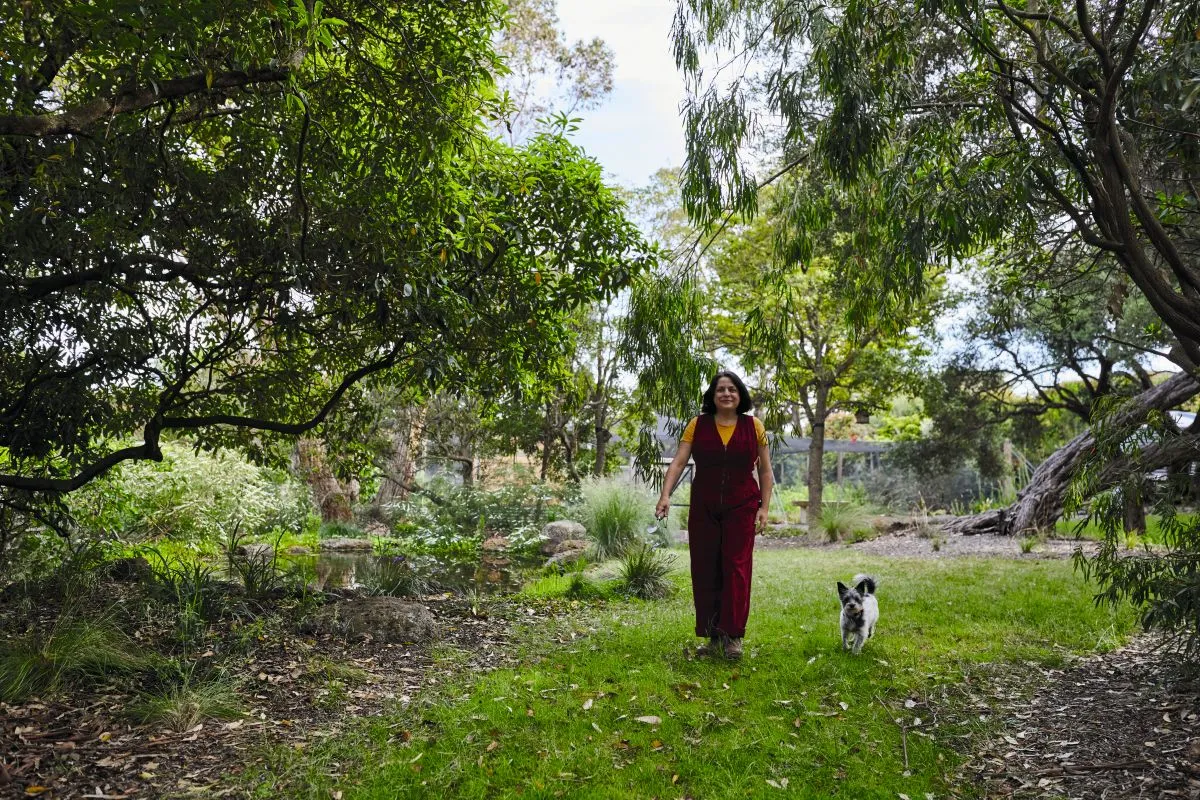 A woman in a red dress walks her dog in a garden.