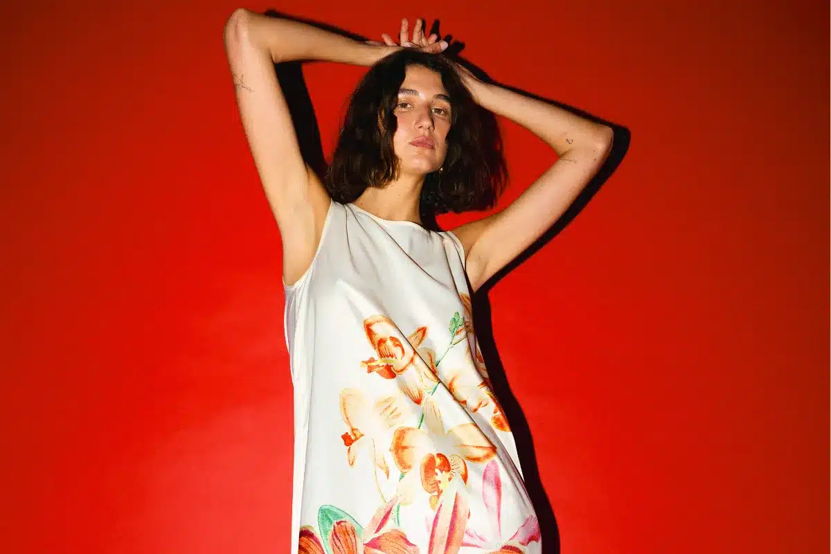 A woman wearing a floral dress stands gracefully, showcasing vibrant flowers against a soft fabric background.