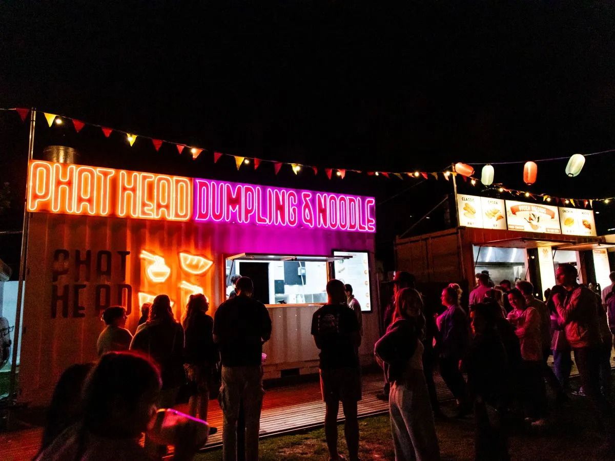 A diverse group of people gathered outside a food truck, enjoying food and conversation in a lively outdoor setting.