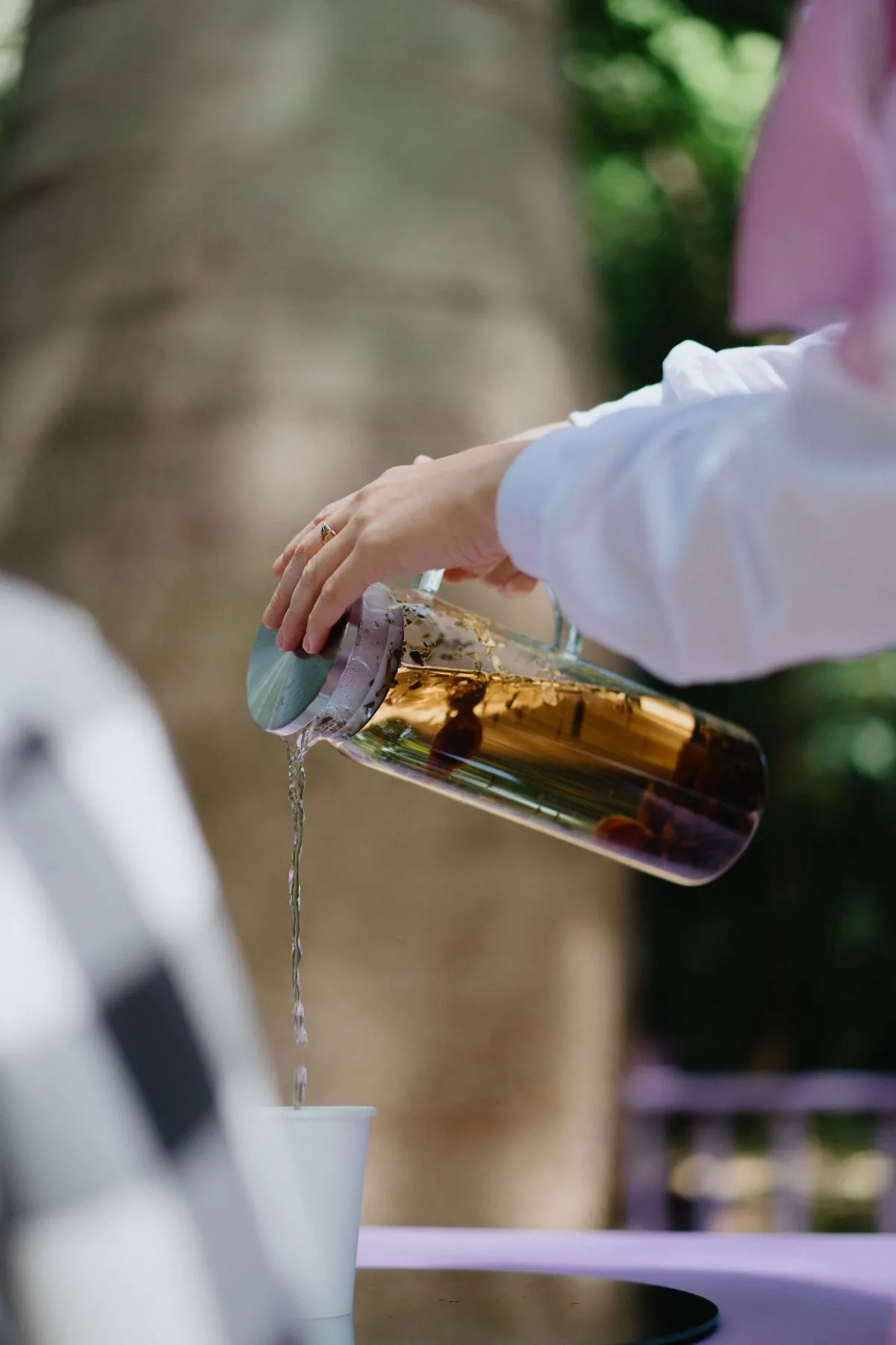 A person pouring steaming tea from a teapot into a delicate cup on a wooden table.