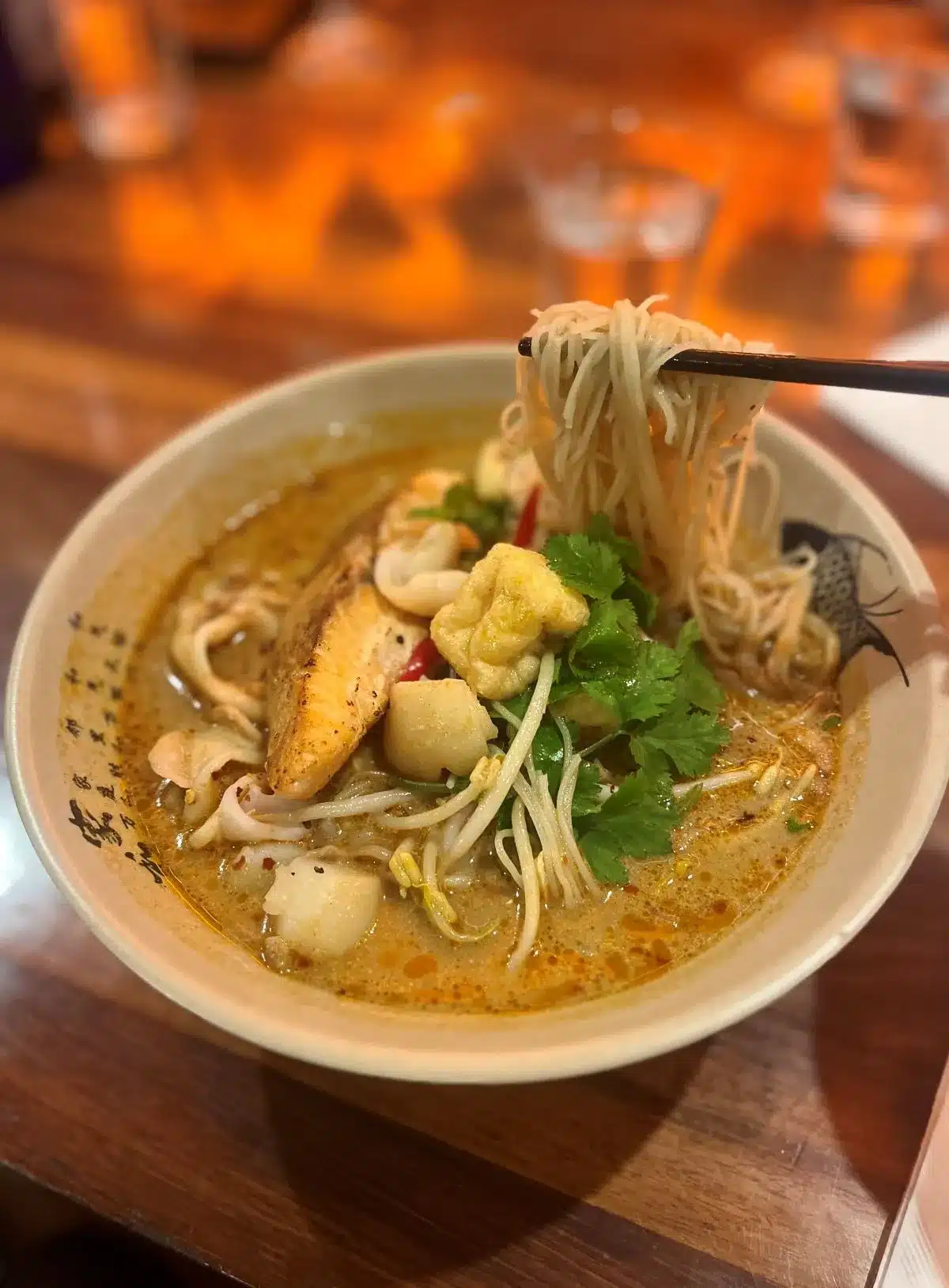 A bowl of noodles topped with a variety of seafood and colorful vegetables, garnished for an appetizing presentation.