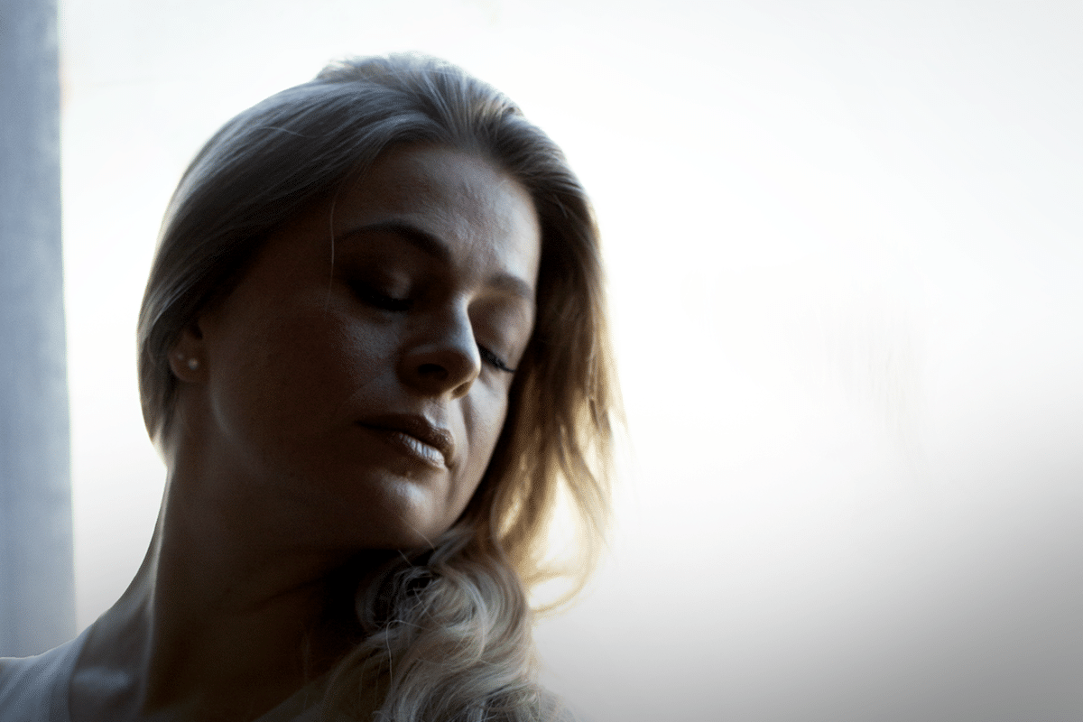 A woman with her eyes closed, appearing serene and contemplative in a peaceful setting.