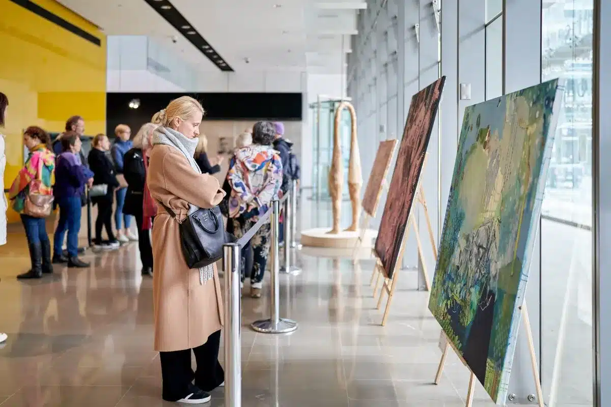 A group of people observing various artworks displayed in a bright, spacious art gallery.