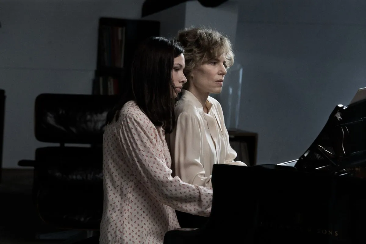 Two women playing a grand piano together in a cozy room filled with warm light and musical notes.