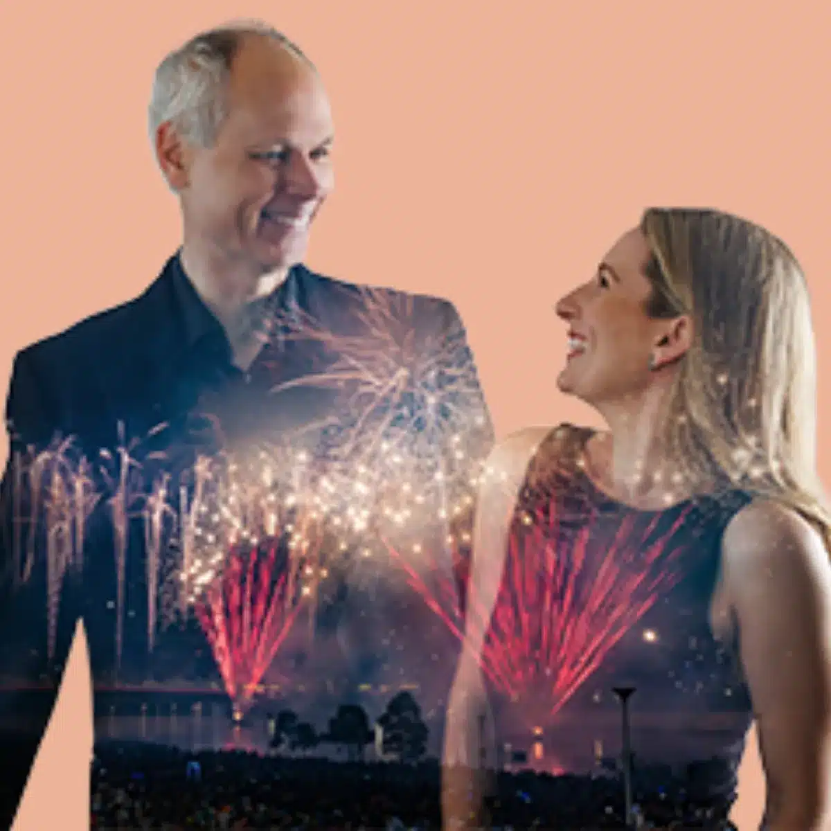 A man and woman stand together, smiling, as colorful fireworks illuminate the night sky behind them.