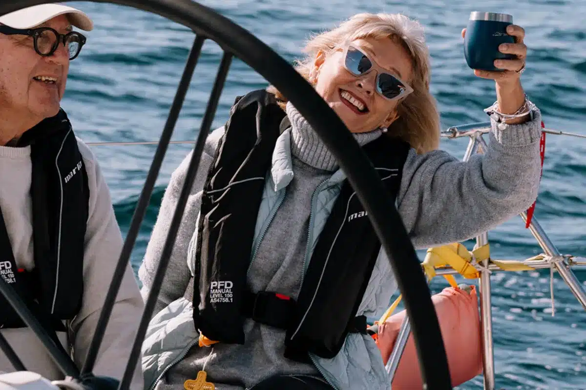 A man and woman enjoy a sunny day sailing on a boat, with the ocean and clear sky in the background.