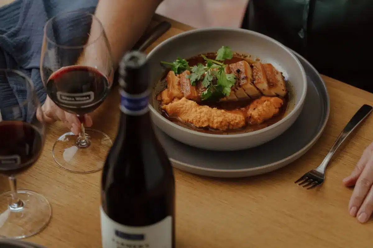A person holding a wine glass in one hand and a plate of food in the other, enjoying a meal.