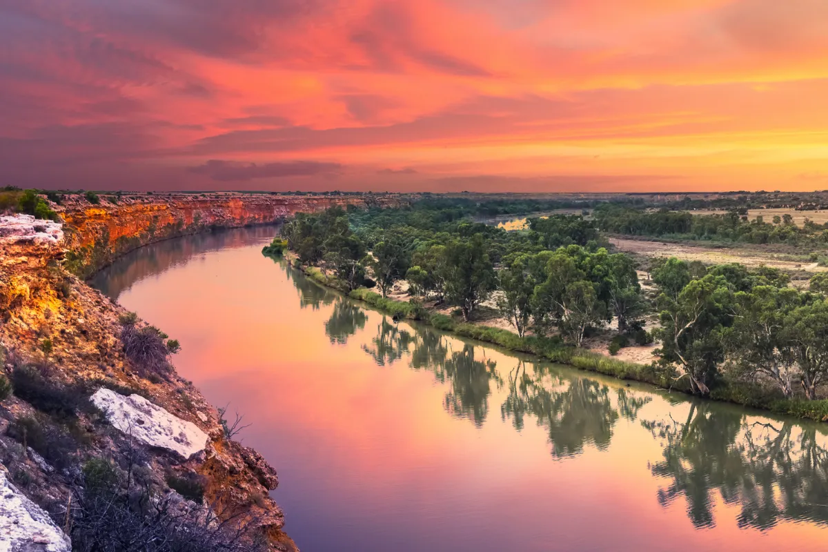 A river flows, illuminated by the warm hues of sunset in the background.