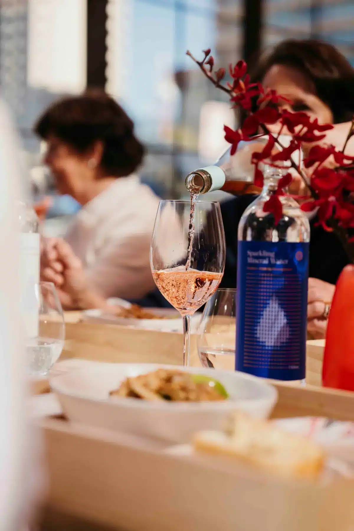 A woman elegantly pours red wine from a bottle into a glass, showcasing a moment of hospitality and celebration.