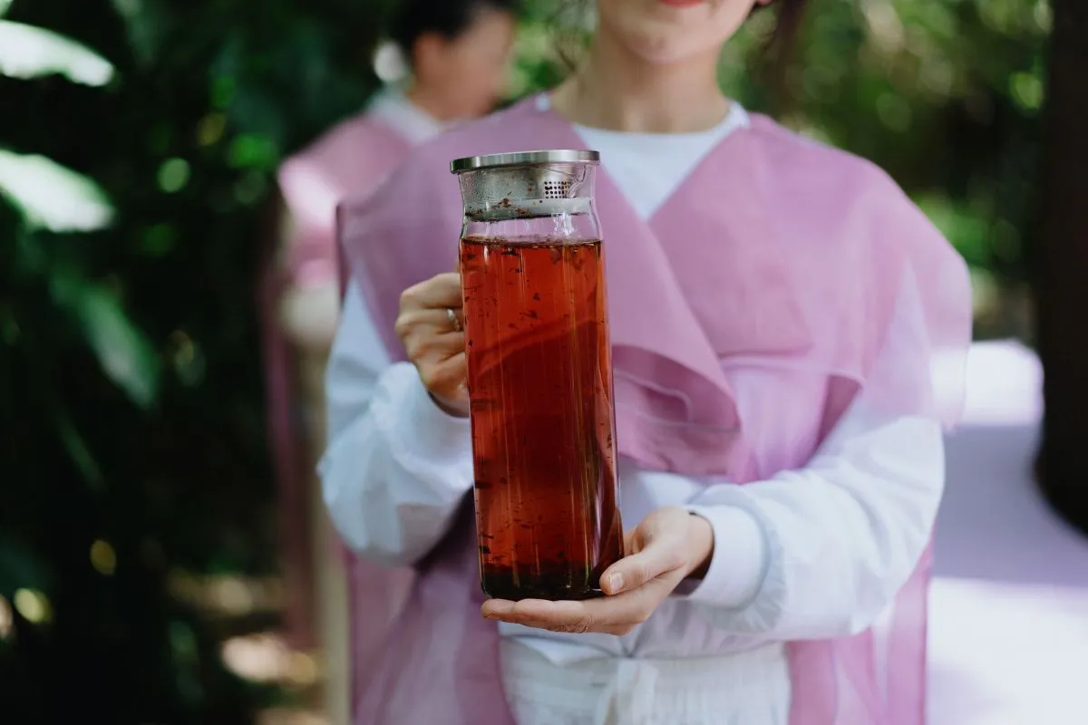 A woman holding a glass of tea, smiling gently as she enjoys her drink.