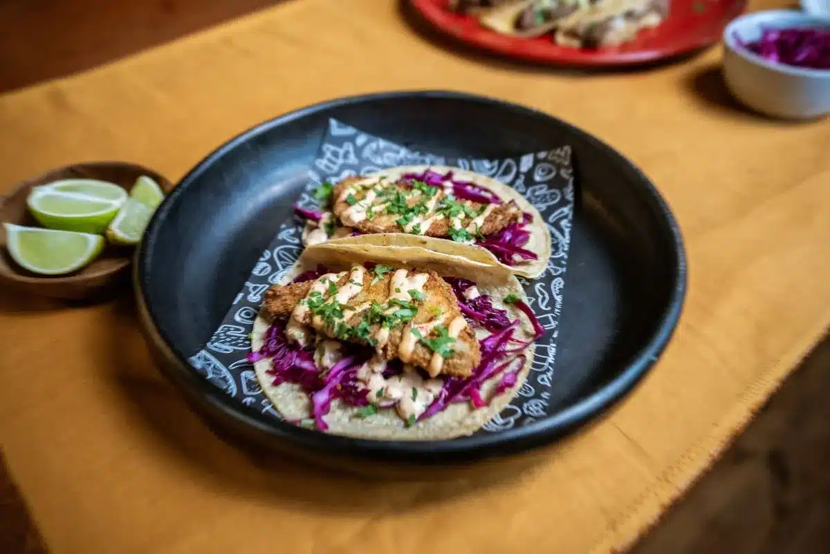 Two tacos on a plate, garnished with red cabbage and lime wedges, ready to be enjoyed.