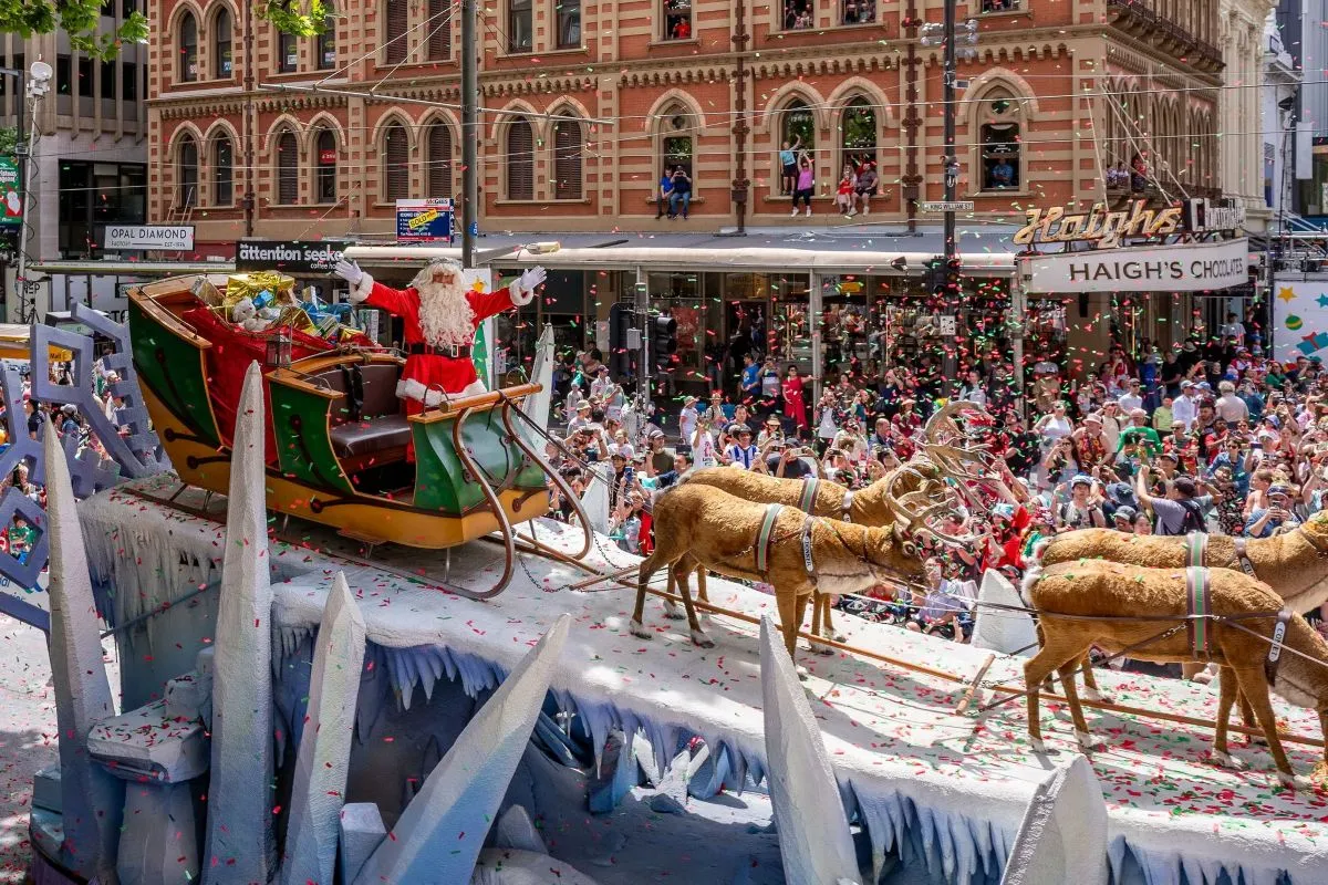 A festive parade float featuring Santa Claus surrounded by reindeer, decorated with colorful lights and holiday ornaments.