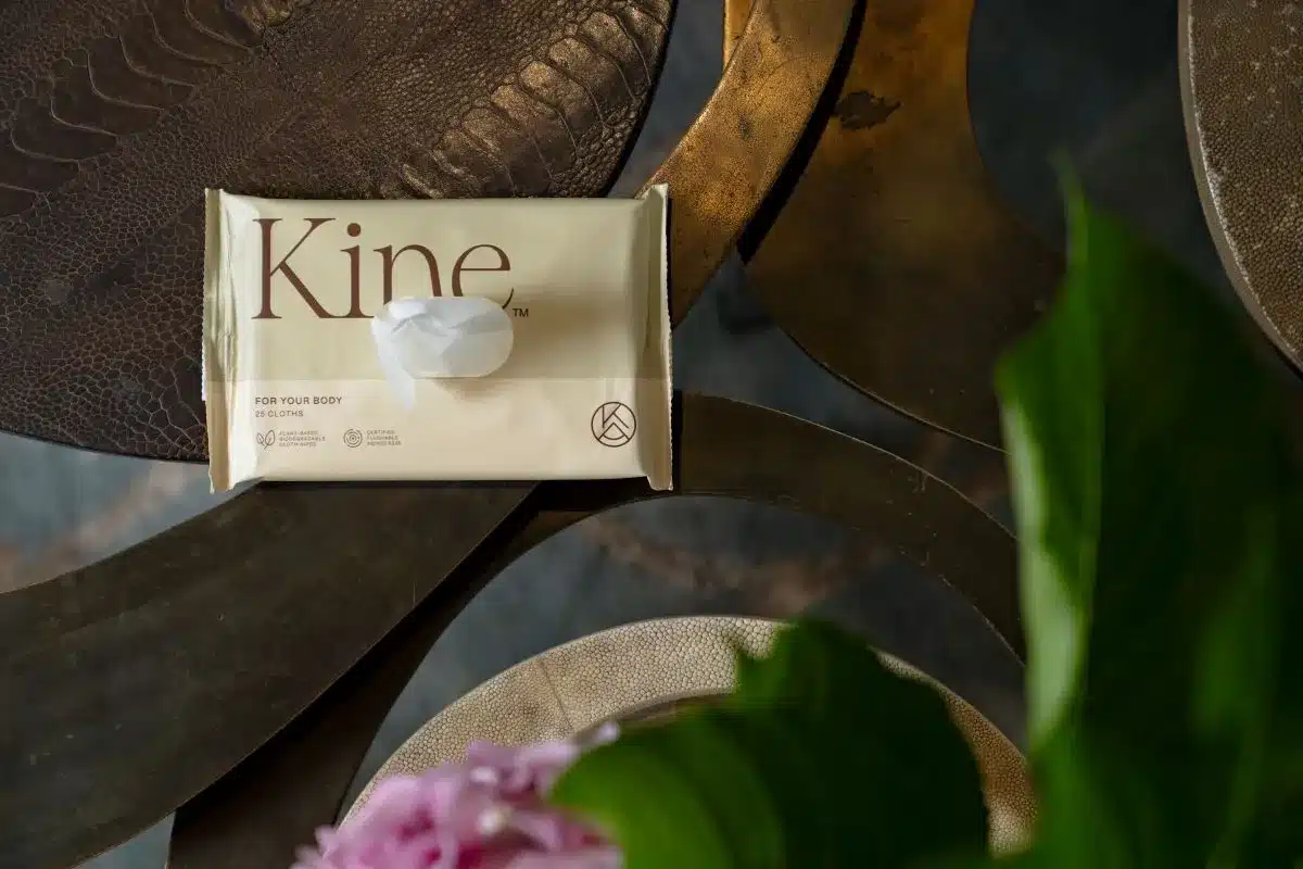 A packet of Kine rests on a table beside a colorful vase filled with fresh flowers.