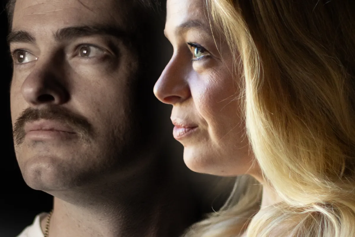A man with a mustache and a woman gaze at each other, sharing a moment of connection and understanding.