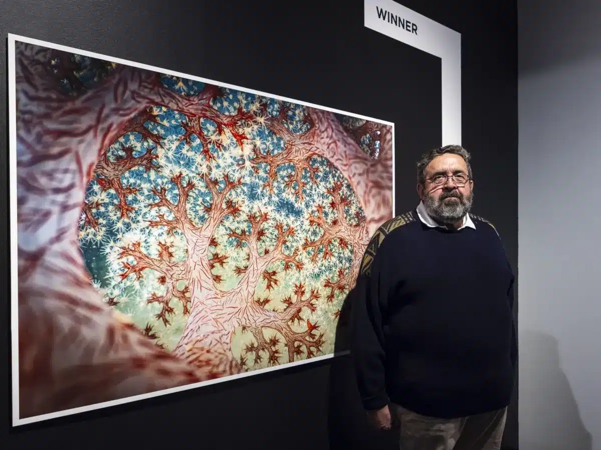 A man stands beside a large photograph.