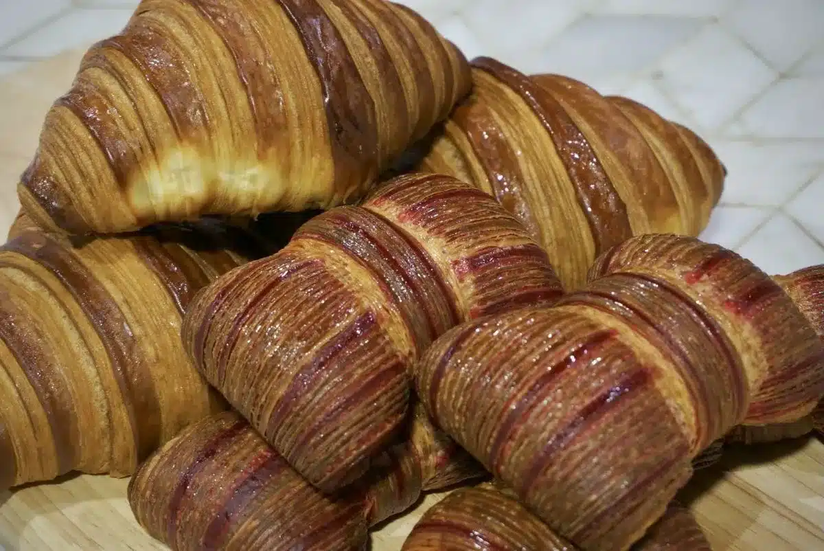 A stack of golden-brown croissants rests on a wooden cutting board, showcasing their flaky texture and inviting appearance.