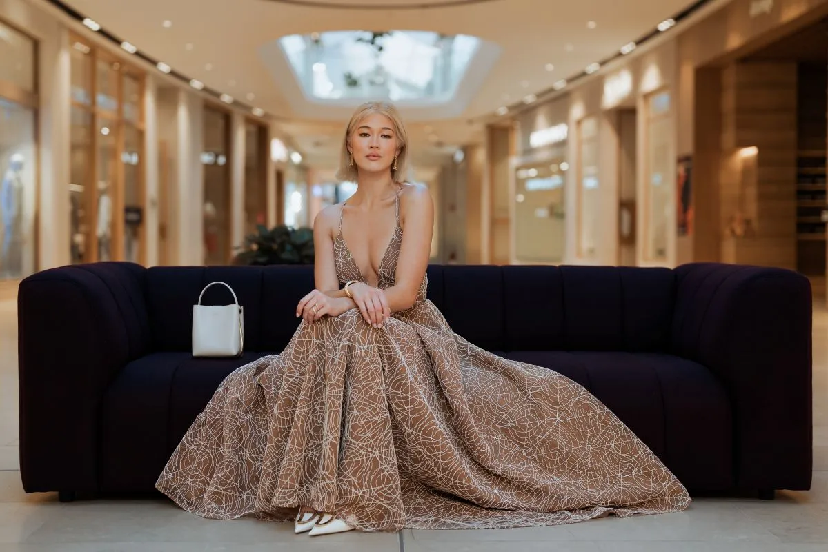 A woman in a long dress sits gracefully on a couch, exuding elegance and comfort in her relaxed pose.