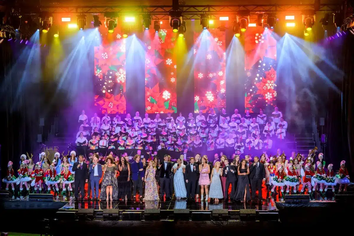 A group of people stands on stage, illuminated by bright lights, engaging with an audience.