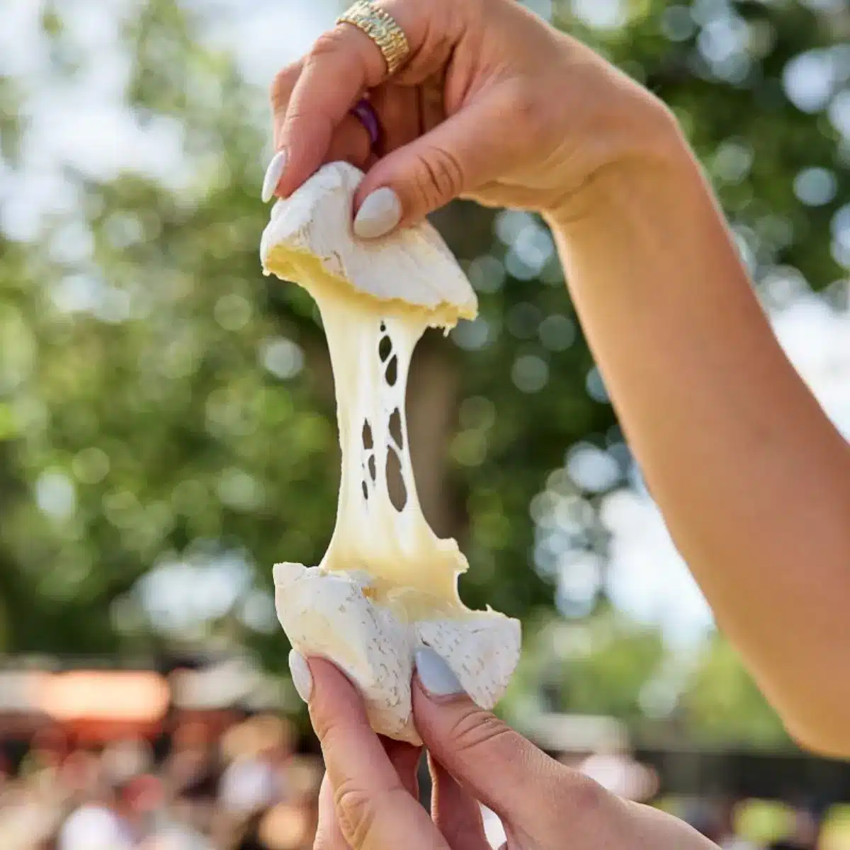 A person holding a piece of cheese, stretching it with their fingers.