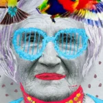 An elderly woman with colorful glasses and small birds perched on her head, smiling gently at the viewer.