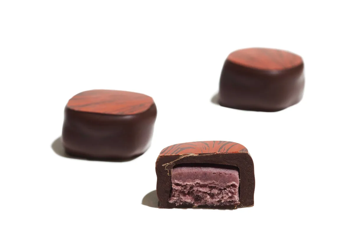 Three pieces of chocolate with a creamy pink filling arranged on a white plate.