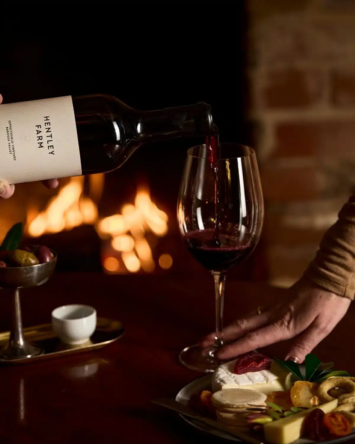 A person pouring red wine from a bottle into a glass on a table, with a soft focus on the wine's rich color.