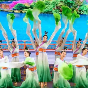 A group of women in green dresses performing energetically on stage, showcasing their talent and coordination.