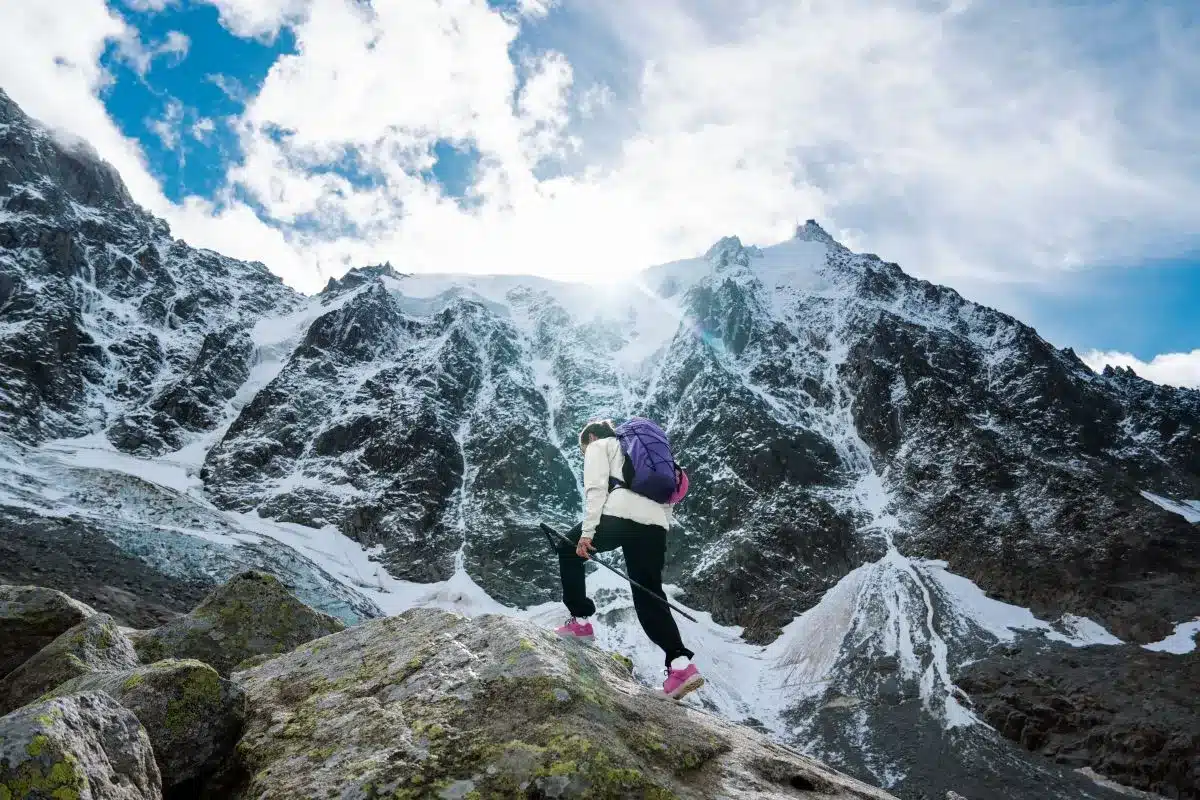 A woman with a backpack stands on a mountain, enjoying the scenic view around her.