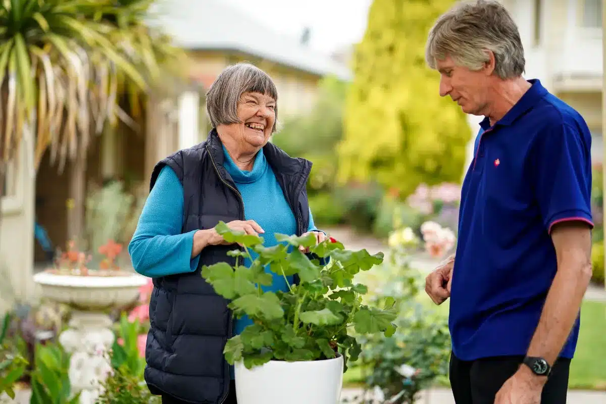 An older woman receives help from a support worker in the garden.