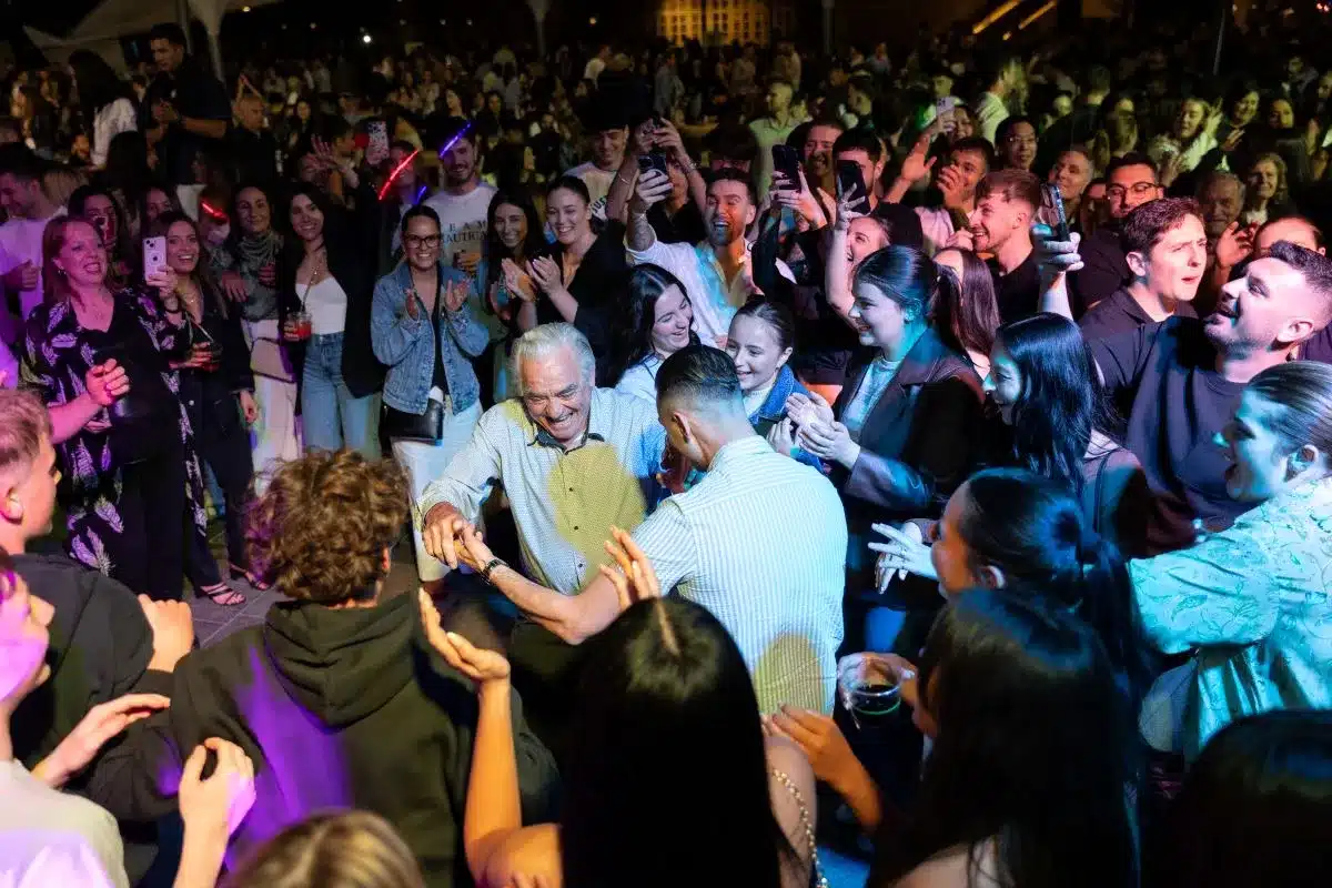 A lively crowd of people dancing joyfully at a vibrant party, with colorful lights illuminating the scene.
